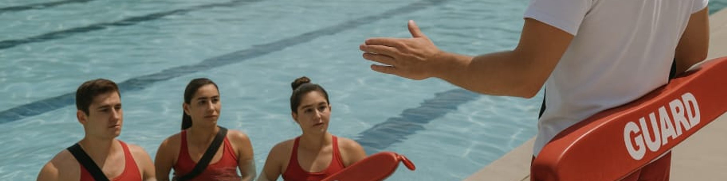 Lifeguard instructor briefing three lifeguard candidates in the pool